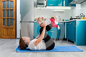A happy mother holds a baby in her arms while having fun doing fitness together on a mat. The concept of home sports training with