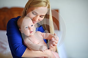 Happy mother holds on hands of the newborn baby, smiles and presses to a breast