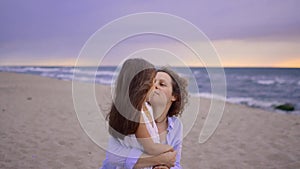 Happy mother is hugging baby on seaside beach at sunset.