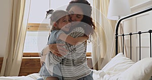 Happy mother hugging cute little child daughter playing on bed