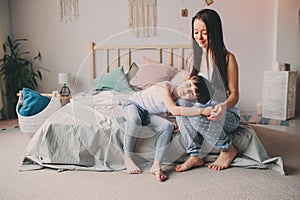 Happy mother hugs her toddler son in the morning, sitting on bed at home.