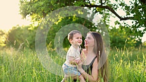 Happy mother hugs and whirls with her little son in park. Young mom and her baby son in a green park having fun. Happy