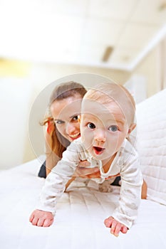 Happy mother and interested baby playing on divan