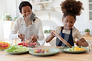 Happy mother and kid sharing cooking chores, preparing salad