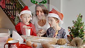 Happy mother with kids celebrating Christmas cooking on kitchen decorated with garlands and baubles. Winter holidays