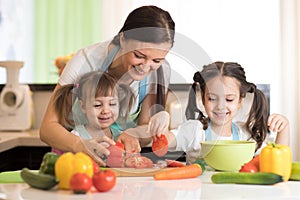 Happy mother and kids cooking and cutting vegetables on kitchen