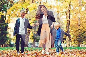 Happy mother and kids having fun outdoors. Fashionable family walking in autumn park