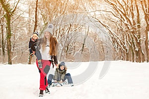 Happy mother and kids having fun with sledge in winter park. Family concept. Winter holidays