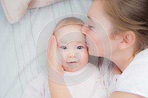 Happy mother kisses baby lying on the bed. Top view