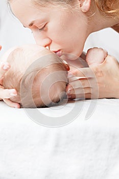 Happy mother kissing a baby, lying on a white bed