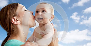 Happy mother kissing little baby over blue sky