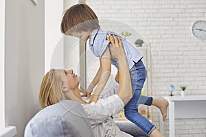 Happy mother lifting her son up into air at home. Parent playing game with little child, having fun in living room