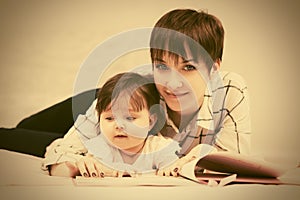 Happy mother and little baby girl reading a book on bed