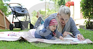 Happy mother and little baby girl reading book together on blanket