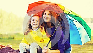 Happy mother and little child with colorful umbrella in sunny autumn park