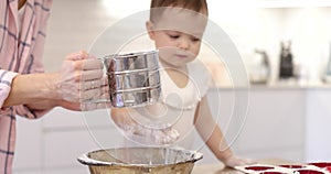 happy mother and little child girl sieving flour into bowl.