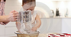 happy mother and little child girl sieving flour into bowl.