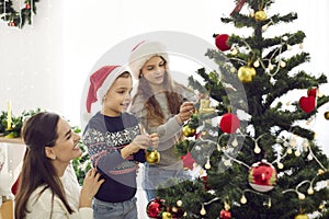 Happy mother and little children hanging ornaments on their Christmas tree together