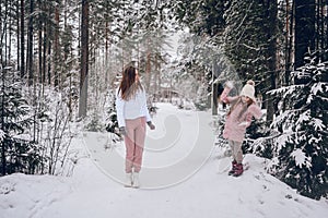 Happy mother and little cute girl in pink warm outwear walking playing snowball fight having fun in snowy white winter