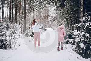 Happy mother and little cute girl in pink warm outwear walking playing snowball fight having fun in snowy white winter