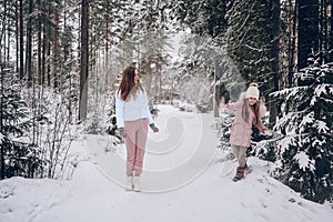 Happy mother and little cute girl in pink warm outwear walking playing snowball fight having fun in snowy white winter coniferous