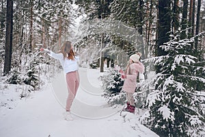 Happy mother and little cute girl in pink warm outwear walking playing snowball fight having fun in snowy white winter coniferous