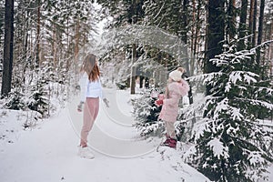 Happy mother and little cute girl in pink warm outwear walking playing snowball fight having fun in snowy white winter coniferous