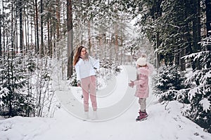 Happy mother and little cute girl in pink warm outwear walking playing snowball fight having fun in snowy white winter coniferous