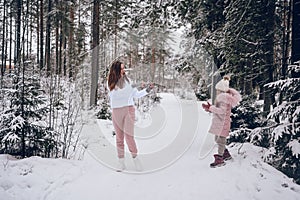 Happy mother and little cute girl in pink warm outwear walking playing snowball fight having fun in snowy white winter coniferous