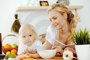 Happy mother and little daughter cooking in kitchen. Spending time all together, family fun concept