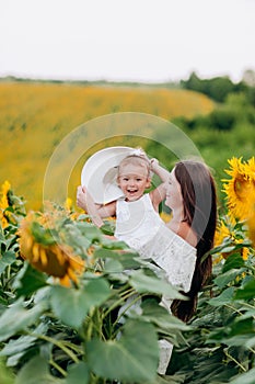 Happy mother with the little daughter in the field of sunflowers. mom and baby girl in mom`s hat having fun outdoors. family