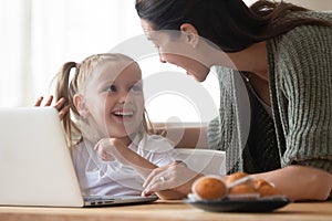 Happy mother and little daughter having fun with laptop