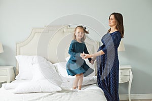 Happy mother and little daughter jumping on the bed