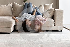 Happy mother and little daughter lying upside down on couch