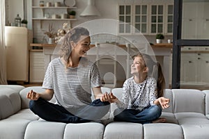 Happy mother with little daughter meditating, practicing yoga together