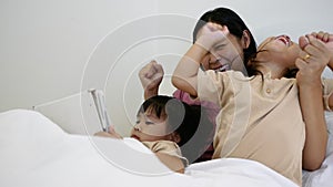 Happy mother and little daughters playing tablet pc computer on bed at night. Happy family time.