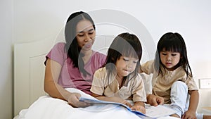 Happy mother and little daughters playing tablet pc computer on bed at night. Happy family time.