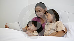 Happy mother and little daughters playing tablet pc computer on bed at night. Happy family time.