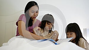 Happy mother and little daughters playing tablet pc computer on bed at night. Happy family time.