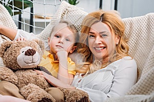 Happy mother and little son laying in hammock with teddy