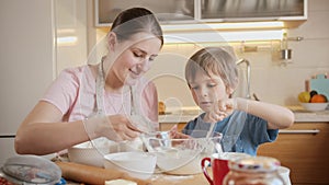 Happy mother with little son stirring and mixing dough ingredients in big glass bowl. Children cooking with parents