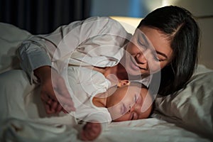 happy mother looking with her infant baby sleeping on bed at night