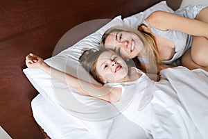 Happy mother lying in bed with little jocund daughter.