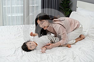 happy mother lying and playing with her infant baby on bed