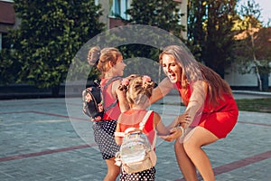 Happy mother meeting her kids daughters after classes outdoors primary school. Family hugging. Back to school