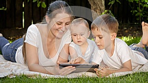 Happy mother with older and baby son browsing internet in park on tablet computer. Parenting, family, children