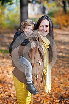 Happy mother piggybacking her son in autumn.