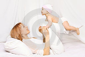 Happy mother playing with baby having fun together on the bed