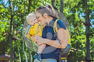 Happy mother playing with baby in the park in autumn. Kid smiling at mum on hands at the park in autumn