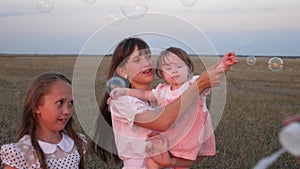 Happy mother playing with children blowing soap bubbles. children catch bubbles and laugh in the park in summer. Slow